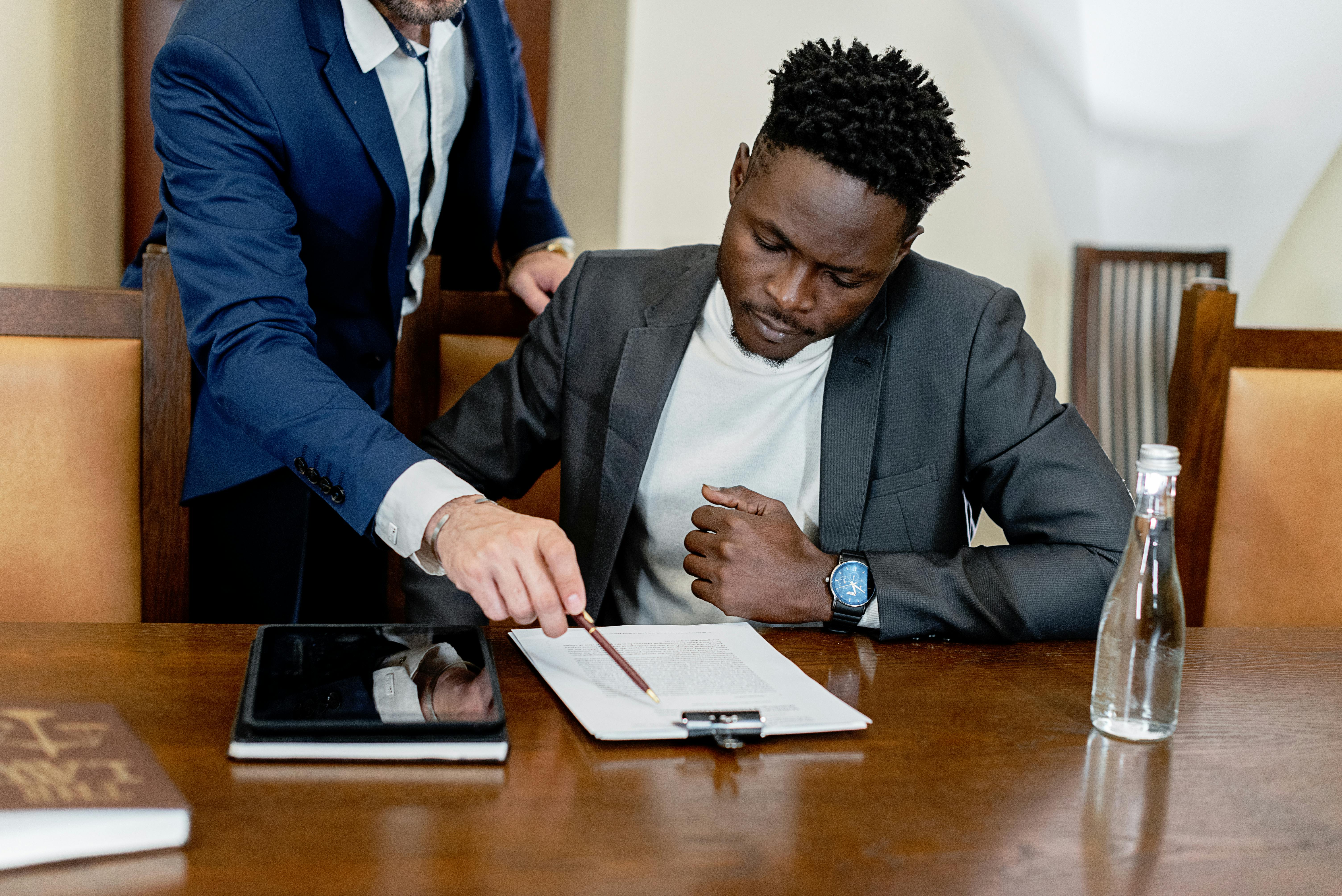 Two businessmen in a legal consultation reviewing a document with a tablet on the desk.